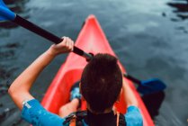 High angle back view of sportswoman padding in red canoe on river water — Stock Photo
