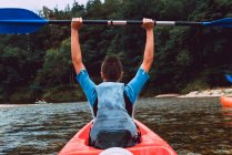Visão traseira da esportista sentada na canoa vermelha e levantando remo depois de ganhar em competição no declínio do rio Sella na Espanha — Fotografia de Stock