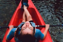 Высокий угол обзора спортсменки сидящей в красном каноэ с закрытыми глазами на речной воде — стоковое фото