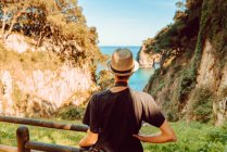Vista trasera de mujer en sombrero de pie junto a barandilla de madera y disfrutando de impresionantes vistas al mar y acantilados en Ribadedeva Asturias España - foto de stock