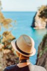 Rückenansicht einer Frau mit Hut, die an einem Holzgeländer steht und einen atemberaubenden Blick auf das Meer und die Klippen in Ribadedeva Asturias genießt — Stockfoto