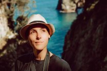 Молода жінка в капелюсі стоїть з камерою, що висить на шиї і насолоджується мальовничим видом на море і скелі в Рібадедедева - Астурія (Іспанія). — стокове фото