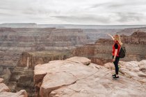 Jeune femme avec sac à dos pointant vers la vue pittoresque du canyon aux États-Unis — Photo de stock
