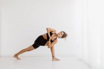 Fitte Frau in Twist-Yoga-Pose vor weißem Hintergrund — Stockfoto