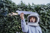 Excited boy in astronaut helmet playing with paper plane with petard in garden — Stock Photo