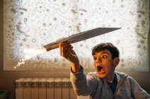 Amüsierter Junge spielt mit Papierflugzeug mit Petard im Zimmer — Stockfoto