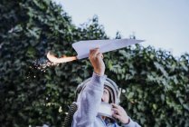 Garçon excité dans un casque d'astronaute jouant avec un avion en papier avec pétard dans le jardin — Photo de stock