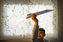 Зачарований хлопчик грає з паперовим літаком з пером у кімнаті — стокове фото