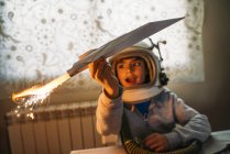 Fantasierender Junge im Astronautenhelm spielt zu Hause mit Papierflieger — Stockfoto