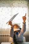 Fantaseando chico en casco astronauta jugando con avión de papel en casa - foto de stock