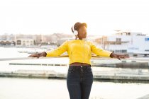 Афроамериканка в модном пиджаке слушает музыку в наушниках, опираясь на стеклянный балкон — стоковое фото