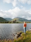 Людина стоїть біля води і насолоджується мальовничим пейзажем з зеленими скелями і середньовічним замком Кілчтерн в сонячний день. — стокове фото