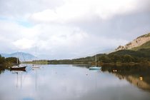 Paisaje pintoresco de montaña y cielo nublado reflejado en aguas tranquilas con veleros en Glencoe durante el día. - foto de stock