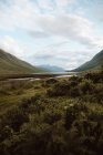 Paisagem idílica de altas montanhas verdes e vale com rio tranquilo sob céu nublado em Glen no verão — Fotografia de Stock