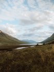 Paisagem idílica de altas montanhas verdes e vale com rio tranquilo sob céu nublado em Glen no verão — Fotografia de Stock