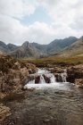 Breathtaking view of high bare mountains and water falling from rock into Fairy Pool on daytime — Stock Photo