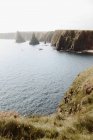 Desde arriba impresionante paisaje de formaciones de roca en forma de cono en el agua por costa en Duncansby Head el día soleado. - foto de stock