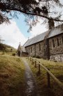 De abaixo da estrada com grade de madeira que conduz até o monte verde com a igreja histórica de Nantgwyllt no dia — Fotografia de Stock