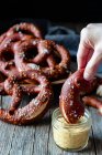 Crop person immergendo pretzel fresco fatto in casa con sale in salsa di formaggio sulla tavola di legno — Foto stock