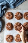 Von oben Person Hand anfassen köstliche Schokolade Brownie Cookies auf weißem Pergament durch blaues Handtuch — Stockfoto