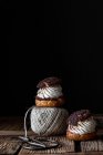 Pasticcini fatti in casa con forbici crema e cioccolato e gomitolo di filato disposti su superficie di legno texture su sfondo nero — Foto stock