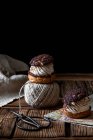 Pâtisseries maison choux avec ciseaux crème et chocolat et boule de fil disposée sur une surface en bois texture sur fond noir — Photo de stock
