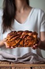 Кукурудза жіноча кухарка тримає свіжий скручений хліб або корицю бабка над дерев'яним столом зі смугастим рушником на розмитому фоні — стокове фото