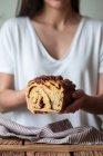 Cultivo cozinheiro feminino segurando pão fresco torcido ou canela babka sobre mesa de madeira com toalha listrada no fundo borrado — Fotografia de Stock