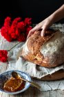 Persona irriconoscibile che mette pane di pasta madre su tavolo rustico vicino a nido d'ape e mazzo di garofani rossi — Foto stock
