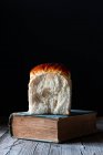 Bollo de pan fresco en libro vintage colocado sobre mesa de madera . - foto de stock