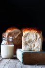 Невелика банка свіжого молока і булочки запеченого хліба на старій книзі рецептів, розміщеній на дерев'яному столі . — стокове фото