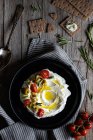 Верхняя тарелка йогурта лабне с помидорами и оливками на деревянном столе рядом с салфеткой, ложкой и хрустящими крабовыми палочками и соусом эмари — стоковое фото