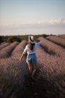Vista trasera de chica casual en sombrero caminando en flores de gran campo de lavanda en el campo . - foto de stock