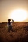 Jovem mulher de pé em flores em grande campo de lavanda no campo ao pôr do sol . — Fotografia de Stock