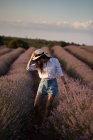 Elegante giovane donna che cammina vicino a fiori in un grande campo di lavanda in campagna . — Foto stock
