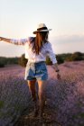 Stilvolles junges Mädchen, das in der Nähe von Blumen in einem großen Lavendelfeld auf dem Land spaziert. — Stockfoto