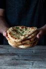 Unrecognizable man holding stack of fresh naan flatbread over lumber table in rustic kitchen — Stock Photo