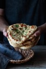 Unrecognizable man holding stack of fresh naan flatbread over lumber table in rustic kitchen — Foto stock
