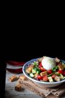 Bowl with yummy panzanella salad placed on cloth on wooden table against black background — Stock Photo