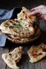 Unrecognizable man holding stack of fresh naan flatbread over lumber table in rustic kitchen — Foto stock