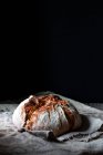 Pain de pain frais au levain de campagne placé sur un morceau de bois sur une table minable sur fond noir — Photo de stock