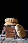 Fresh pita flatbread placed on napkin and wooden blocks on rustic table against black background — Stock Photo