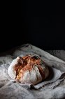 Loaf of fresh country sourdough bread placed on piece of wood on shabby table against black background — Stock Photo