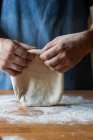 Unerkennbarer Mann in Schürze streicht beim Pizzabacken weichen Teig mit Mehl über den Tisch — Stockfoto