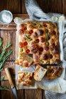Overhead potato focaccia with fresh rosemary placed near bowl with salt and striped napkin on wooden table — Stock Photo