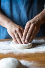 Unrecognizable male in apron flattening soft dough over table with flour while cooking pizza — Stock Photo