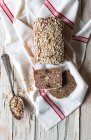 From above loaf of tasty ryecorn bread placed on cloth napkin near spoon of grain on wooden background — Stock Photo