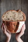 Unbekannter zeigt frisches halbiertes Brot mit Samen gegen Holzwand — Stockfoto