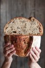 Persona irriconoscibile che mostra pane fresco dimezzato con semi contro parete di legno — Foto stock