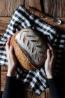 Top view of loaf of fresh spelt bread placed on checkered napkin near tool on lumber table — Stock Photo
